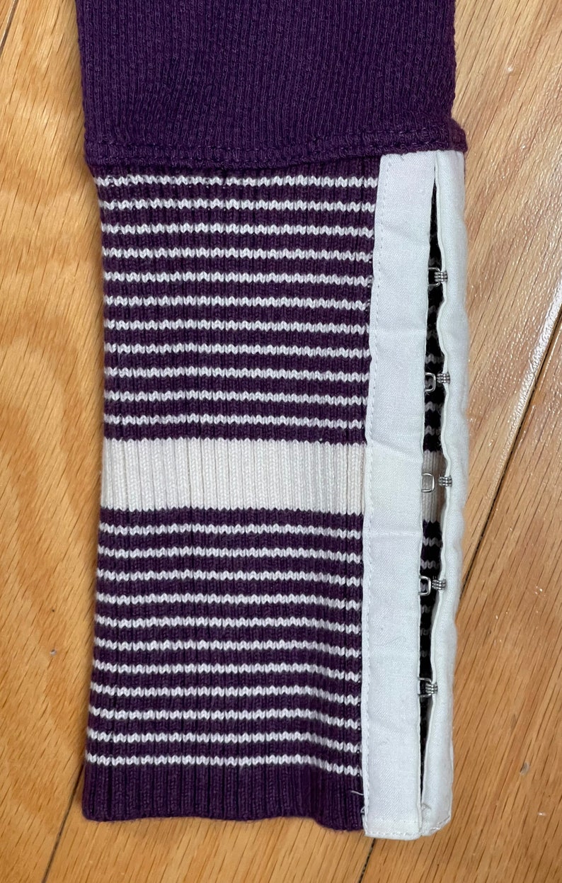 May include: Purple and white striped sweater cuff with a white fabric strip and metal snaps along the side.