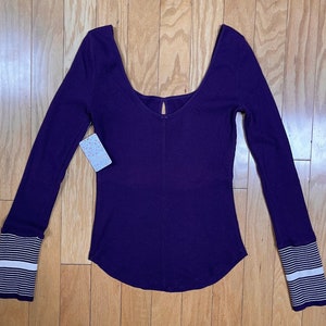 May include: A long-sleeved, purple, ribbed, scoop neck top with white striped cuffs.