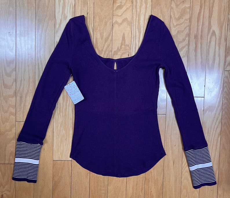 May include: A long-sleeved, purple, ribbed, scoop neck top with white striped cuffs.