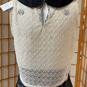 May include: White crochet sleeveless dress with a black Peter Pan collar and a black leather skirt. The dress has a lace pattern and a keyhole back.
