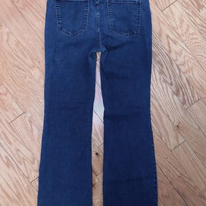 May include: Dark blue denim jeans with a high waist and flared leg. The back view shows two pockets and a classic jean design. The jeans are made of a sturdy denim material and are suitable for everyday wear.