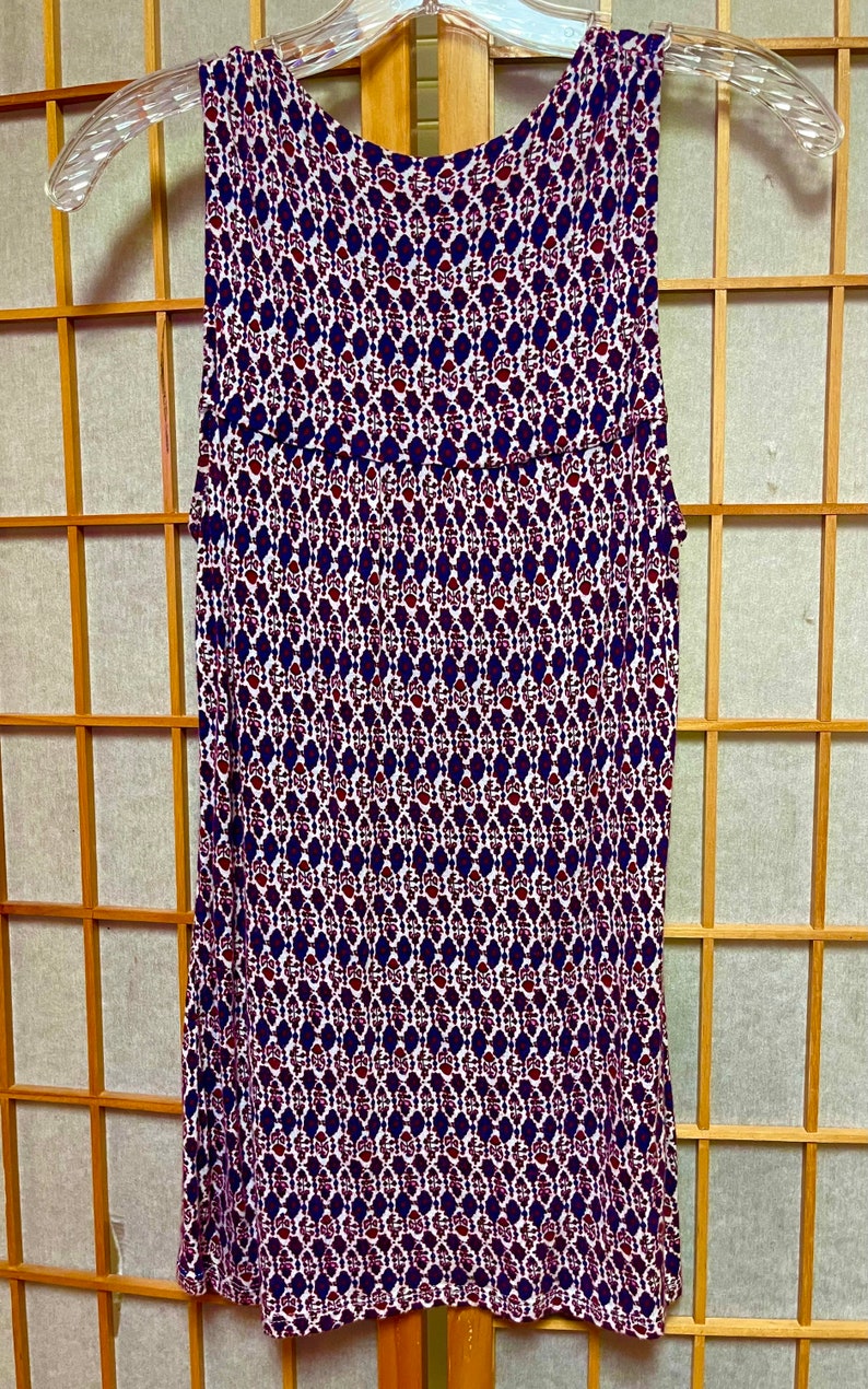 May include: A sleeveless white tank top with a geometric pattern in shades of red, blue, and white.