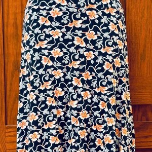 May include: A black skirt with a floral pattern. The design features orange flowers and white vines against a black background. The skirt is knee-length and made of a soft, flowing fabric.