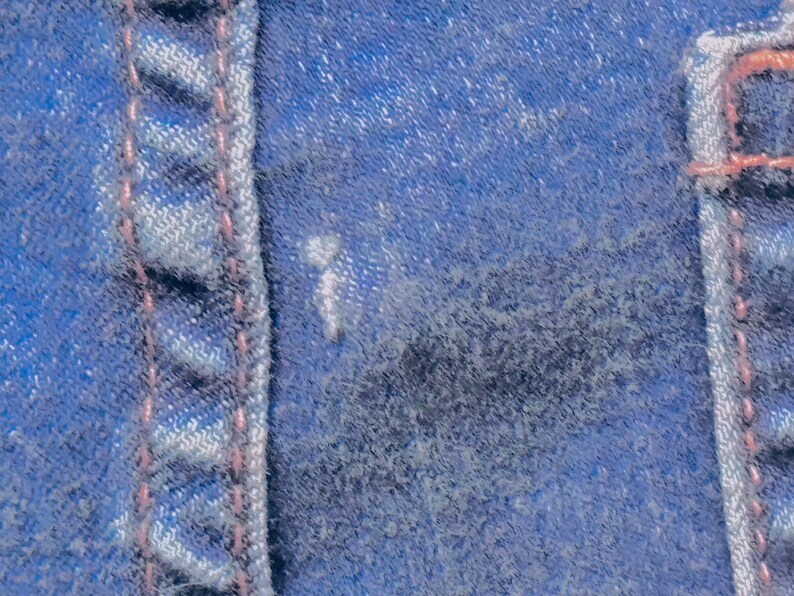 May include: Close-up of blue denim fabric with visible stitching in a lighter blue color and pink thread. The texture of the denim is rough and worn, with a few light spots.