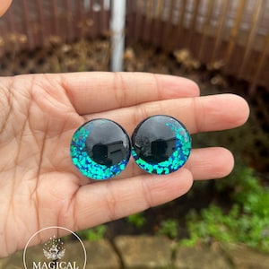 May include: Two round black and green glitter eyes with a black center. The eyes are about 1 inch in diameter.