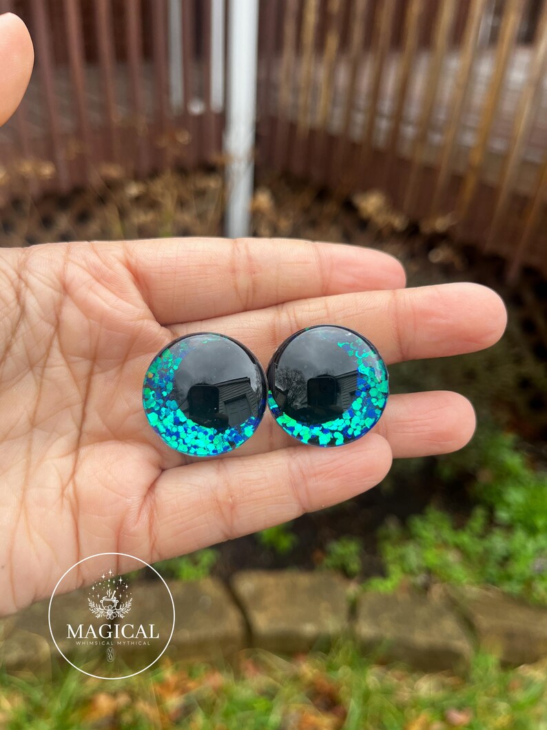 May include: Two round black and green glitter eyes with a black center. The eyes are about 1 inch in diameter.