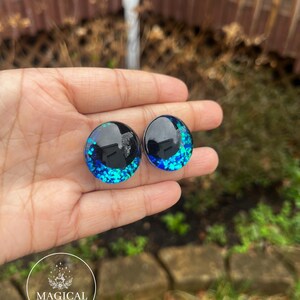 May include: Two round black and blue glitter resin eyes with a black rim. The eyes are approximately 1 inch in diameter.