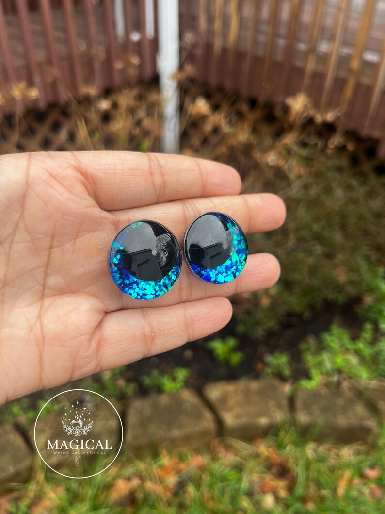 May include: Two round black and blue glitter resin eyes with a black rim. The eyes are approximately 1 inch in diameter.