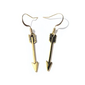 May include: A pair of gold arrow earrings with black accents. The arrows are pointing downwards.