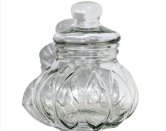 May include: A clear glass jar with a lid, featuring a textured, ribbed design. The jar has a round, bulbous shape and a wide mouth.