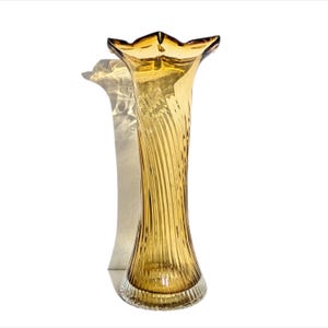 May include: A tall amber glass vase with a flared opening and a swirling, textured design. The vase has a clear glass base.