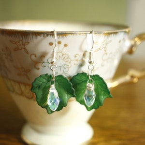 May include: A pair of silver earrings with green leaf-shaped charms and iridescent crystal drops.