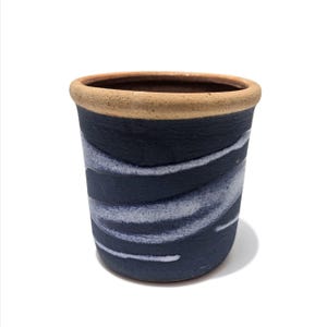 May include: A handmade ceramic tumbler with a dark blue exterior and a light beige rim. The dark blue surface features a wavy, white pattern. The tumbler is a cylindrical shape and sits on a white background.