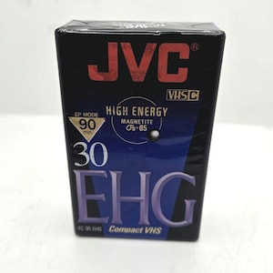 Könnte beinhalten: Eine schwarze JVC VHS-C Videokassettenbox. Die Box zeigt das JVC-Logo in Rot, den Text "HIGH ENERGY" und "EHG". Die Box weist auch eine Aufnahmezeit von 90 Minuten und "Compact VHS" auf.