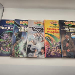 May include: A collection of five vintage "Twistaplot" books. The covers feature colorful illustrations and titles like "The Time Raider" and "The Sinister Studios of Kesp-ty." The books are arranged side by side, showcasing their unique cover art.
