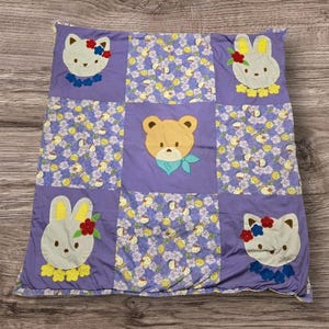 Colcha de retalhos artesanal para bebê, roxa, floral, com apliques de animais: urso, coelho e gato.