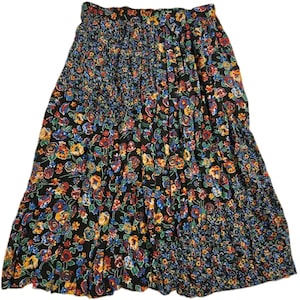 May include: A black midi skirt featuring a vibrant floral pattern with red, yellow, and blue flowers and green leaves. The skirt has a gathered, elasticized waistband and a textured, smocked panel detail on the upper left side and lower right side.
