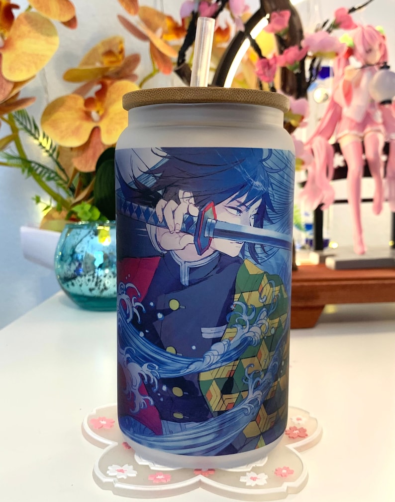 Op de afbeelding: Een witte herbruikbare waterfles met een bamboe deksel en een rietje. De fles heeft een kleurrijk anime-personage met blauw haar en een zwaard. Het personage wordt omringd door blauwe en witte golven.