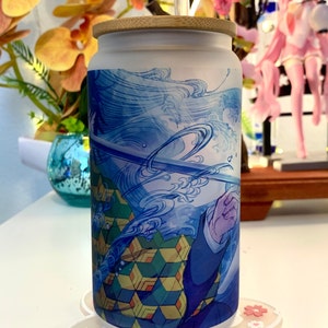 Op de afbeelding: Een witte tumbler met een blauw en groen ontwerp met een personage uit de anime Demon Slayer. De tumbler heeft een bamboe deksel en een rietje.