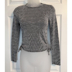May include: A long-sleeve top featuring a black and white checkered pattern. The garment has a crew neckline and includes adjustable side drawstrings at the hem, which create a gathered, ruched effect on both the left and right sides of the waist.