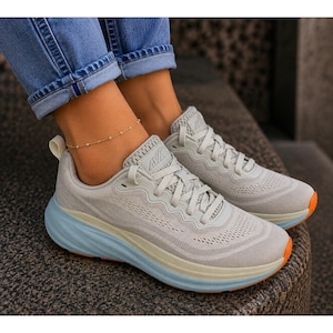 May include: A pair of light gray athletic sneakers featuring a breathable mesh upper, tonal laces, and a thick, light blue cushioned midsole. The outsole has a visible orange accent at the toe, and the Avia brand logo is embossed on the tongue.
