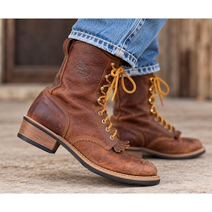 May include: A pair of brown leather work boots featuring a lace-up front with yellow laces, a kiltie fringe detail over the vamp, and a stacked wooden heel with a black rubber sole. The Georgia Boot logo is embossed on the side of the ankle.