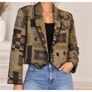 May include: A cropped blazer in olive green and black featuring a geometric tapestry pattern. The jacket has long sleeves, a single button closure, and a notched lapel with black whipstitch detailing along the edges and cuffs.