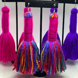 May include: Three pairs of colorful yarn tassel earrings. The earrings are pink, purple, and multi-colored. The tassels are long and fluffy.