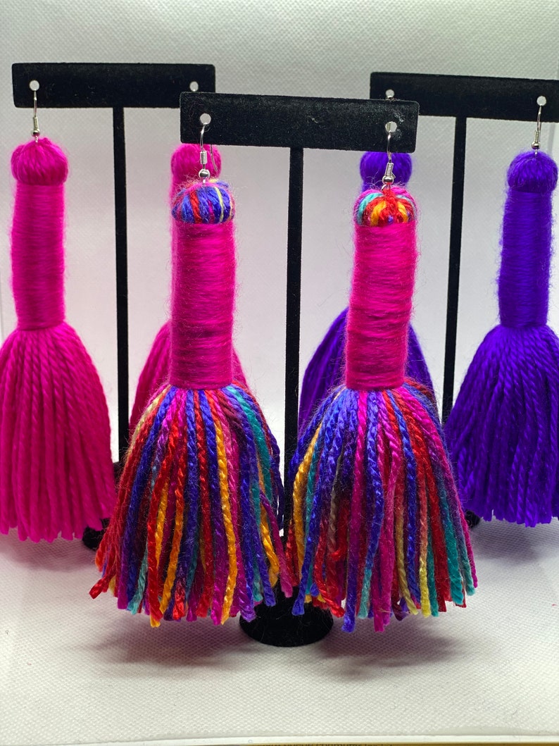 May include: Three pairs of colorful yarn tassel earrings. The earrings are pink, purple, and multi-colored. The tassels are long and fluffy.