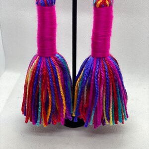 May include: A pair of long, colorful tassel earrings. The tassels are made of yarn in shades of pink, red, blue, green, yellow, and orange. The earrings are suspended from silver hooks.
