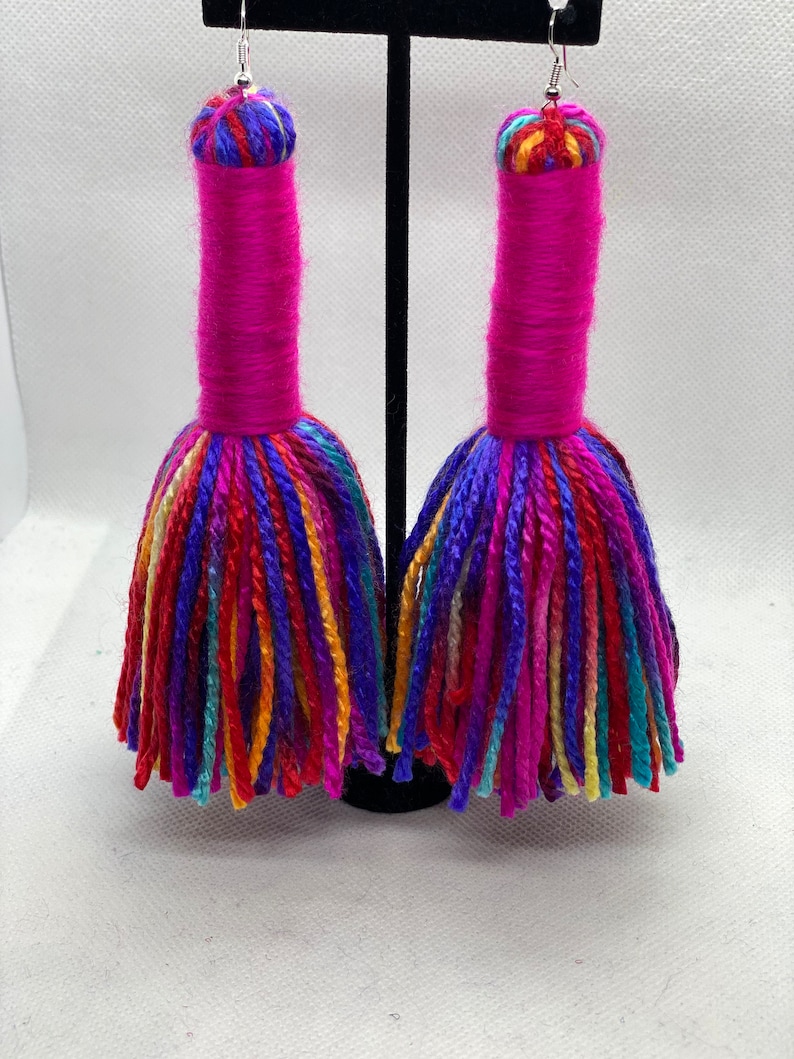 May include: A pair of long, colorful tassel earrings. The tassels are made of yarn in shades of pink, red, blue, green, yellow, and orange. The earrings are suspended from silver hooks.