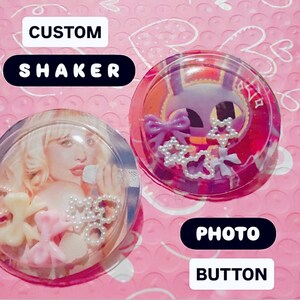 Peut inclure: Deux boutons photo shaker personnalisés circulaires. L'un présente une personne blonde tenant un microphone avec des breloques nœuds rose clair et blancs à l'intérieur. L'autre affiche un personnage violet avec des étoiles et des nœuds.