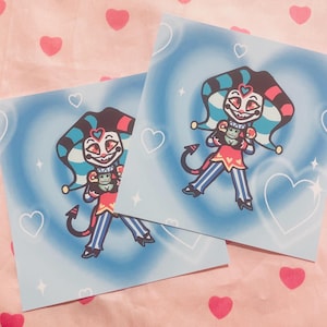 May include: Two square art prints featuring a cartoon jester character with a red, blue, and black color scheme. The background is light blue with white hearts and stars. The prints are on a pink fabric with red hearts.