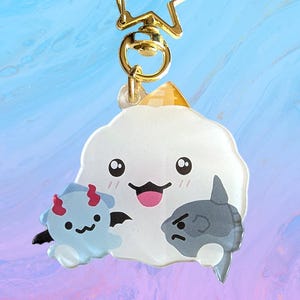 May include: A novelty keychain with a smiling white cloud character, a blue devil, and a grey fish. The charm has a gold-coloured star-shaped clasp. The cloud has a pink tongue.