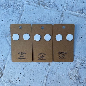 May include: Three sets of white clay earrings on brown card stock with the text "Handmade by Holly Christ" printed on each card.