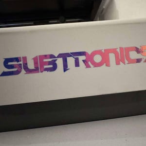 Puede incluir: Una superficie blanca con un logotipo colorido que dice "SUBTRONICS" en una fuente estilizada con colores rosa, azul y naranja.