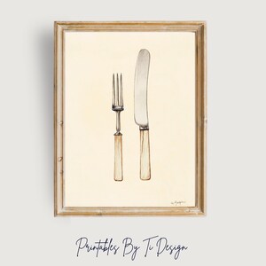 May include: A framed watercolor print featuring a fork and knife. The utensils have silver blades and light-colored handles. The artwork is set against a cream-colored background and is enclosed in a wooden frame. The text "Printables By Ti Design" is at the bottom.