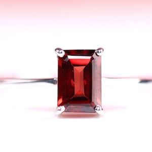 May include: A silver ring with a red gemstone set in a square shape.