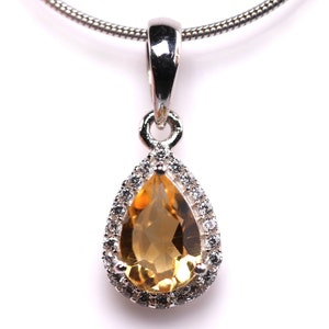 May include: A silver pendant necklace with a teardrop-shaped topaz gemstone surrounded by a halo of smaller clear gemstones.