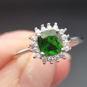 May include: A silver ring featuring a green gemstone set in a halo of smaller white gemstones.