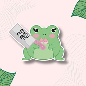May include: A green frog with a pink bow holding a knife with the text "Be kind or else..." on it. The frog is on a pink background with wavy lines.