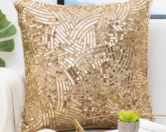 Puede incluir: Una almohada dorada con lentejuelas con un patrón geométrico. La almohada está sentada en un sofá blanco con una manta blanca y una bandeja de madera con una pequeña planta y vasos.