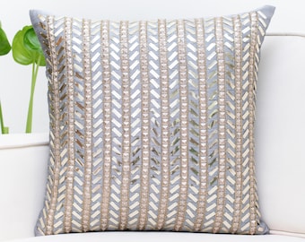 Puede incluir: Una almohada gris con un patrón de chevron bordado con lentejuelas doradas.