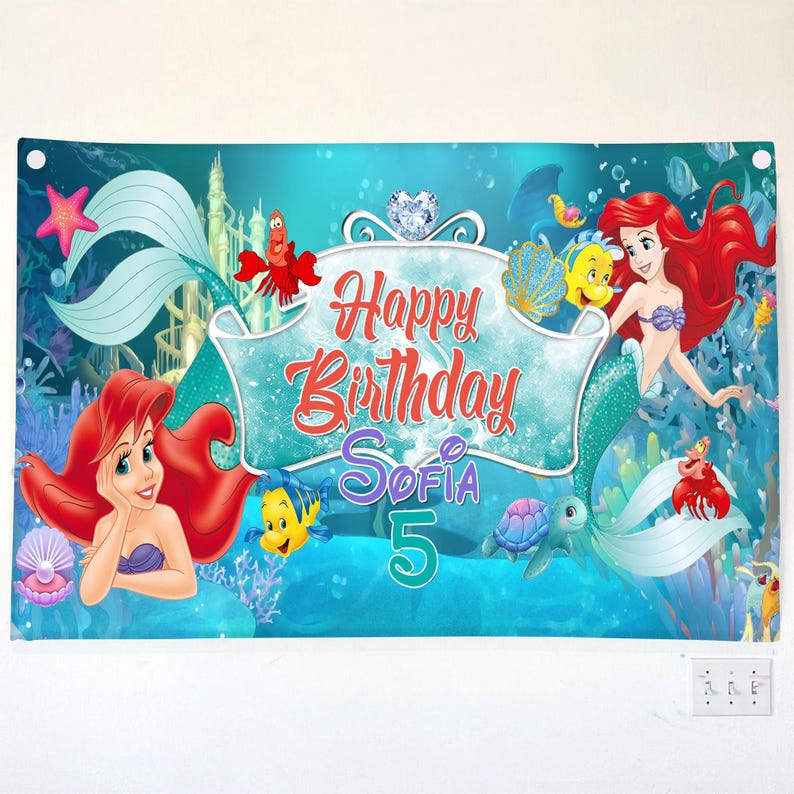 Puede incluir: Una pancarta rectangular con una escena submarina que muestra a la sirena de pelo rojo, un pez amarillo, un cangrejo rojo y una tortuga marina. El texto Happy Birthday Sofia 5 aparece en letras rojas, moradas y turquesas sobre un fondo azul.