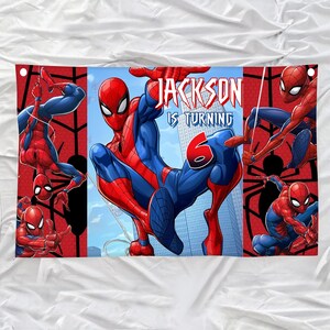Pode incluir: Uma faixa retangular apresentando o Homem-Aranha em v&aacute;rias poses de a&ccedil;&atilde;o contra um c&eacute;u azul e fundo de cidade. O texto diz JACKSON IS TURNING 6 em letras brancas e vermelhas. O design inclui esquemas de cores vermelhas e azuis.