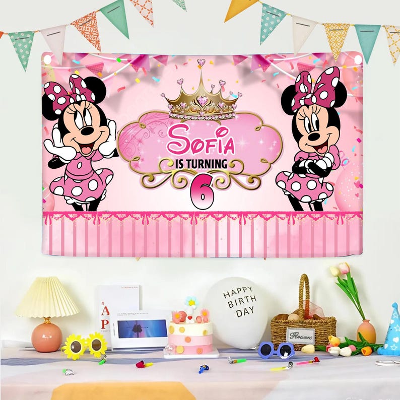 Op de afbeelding: Een roze verjaardagsbanner met Minnie Mouse-illustraties en de tekst "Sofia is turning 6". De banner heeft een kroonontwerp en is versierd met roze strepen en een slinger. Minnie Mouse draagt een roze polkadotjurk en een strik.