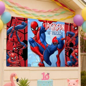 Pode incluir: Uma faixa de anivers&aacute;rio retangular com o Homem-Aranha em trajes vermelhos e azuis contra um fundo de cidade. O texto diz Jackson Is Turning 6. A faixa &eacute; cercada por bal&otilde;es e serpentinas coloridas, com uma figura de flamingo e porco rosa.