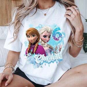 Puede incluir: Camiseta blanca con un dise&ntilde;o de dos princesas animadas, Anna y Elsa, el n&uacute;mero 6 y el nombre "Charlotte". El dise&ntilde;o incluye copos de nieve y detalles en azul hielo, ideal para un cumplea&ntilde;os.