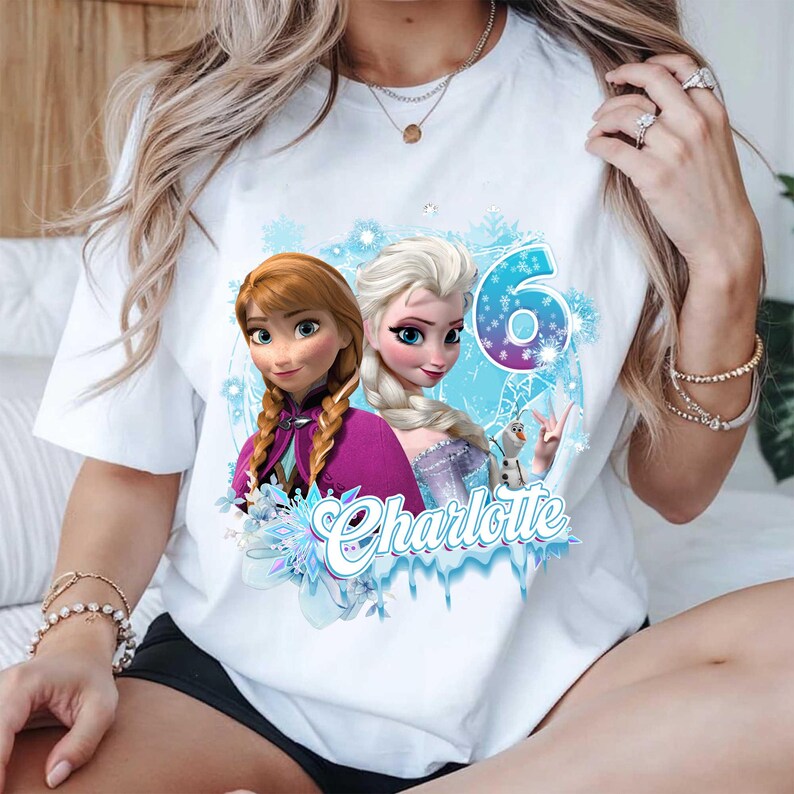 Puede incluir: Camiseta blanca con un dise&ntilde;o de dos princesas animadas, Anna y Elsa, el n&uacute;mero 6 y el nombre "Charlotte". El dise&ntilde;o incluye copos de nieve y detalles en azul hielo, ideal para un cumplea&ntilde;os.