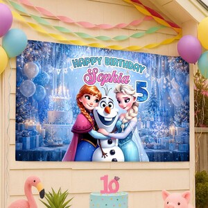 May include: A birthday banner featuring Anna, Elsa, and Olaf from Frozen, with the text "Happy Birthday Sophia 5". The banner is decorated with a winter wonderland scene, balloons, and streamers. A flamingo and a pig figurine are in the foreground.